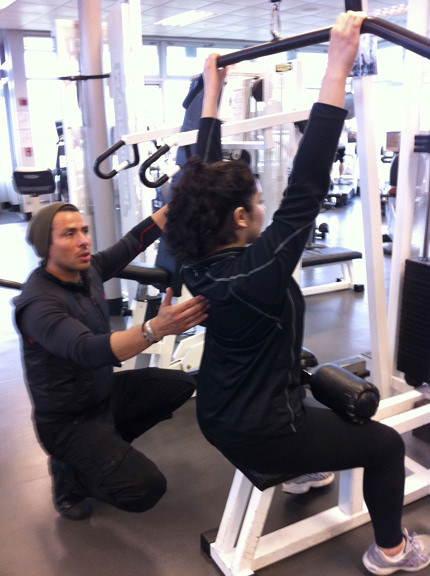 Personal trainer assisting with form on weight training exercise