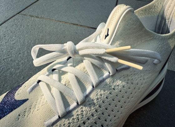 A pair of white Mizuno Neo Vista 2 running shoes with thick, cushioned soles and navy blue accents, placed side by side on a tiled floor in bright natural light, ready for your next review.