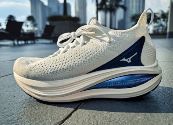 A pair of white Mizuno Neo Vista 2 running shoes with thick, cushioned soles and navy blue accents, placed side by side on a tiled floor in bright natural light, ready for your next review.