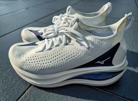A pair of white Mizuno Neo Vista 2 running shoes with thick, cushioned soles and navy blue accents, placed side by side on a tiled floor in bright natural light, ready for your next review.