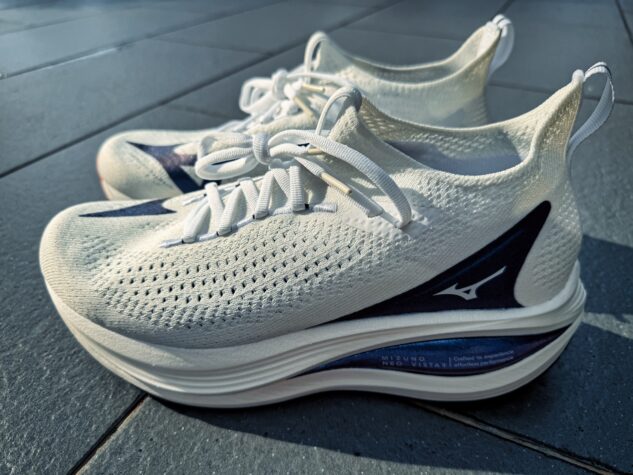A pair of white Mizuno Neo Vista 2 running shoes with thick, cushioned soles and navy blue accents, placed side by side on a tiled floor in bright natural light, ready for your next review.